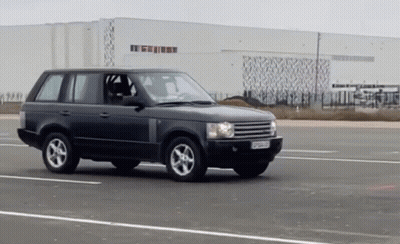 A Black Range Rover Is Driving Down A Road In Front Of A Large White Building GIF