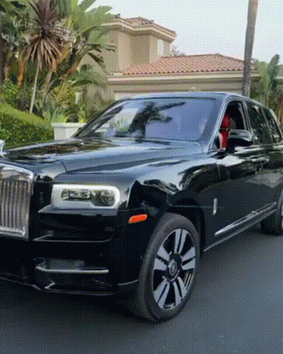 A Black Rolls Royce Is Parked On The Street In Front Of A House GIF