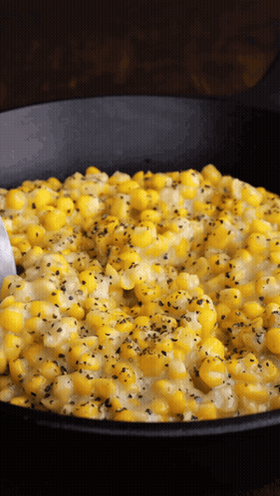 A Black Skillet Filled With Corn And Cheese With A Spoon In It GIF