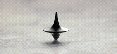 A Black Spinning Top Is Sitting On Top Of A White Surface . GIF