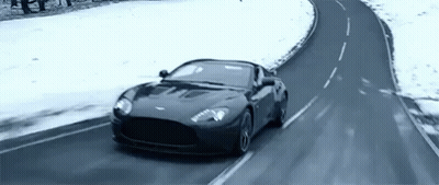 A Black Sports Car Is Driving On A Snowy Road . GIF