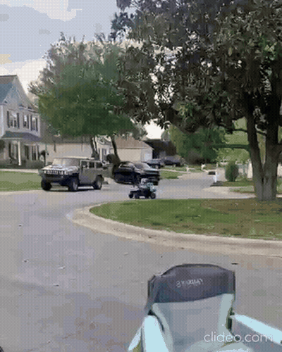 A Black Suv Is Driving Down A Residential Street Next To A Lawn Mower GIF
