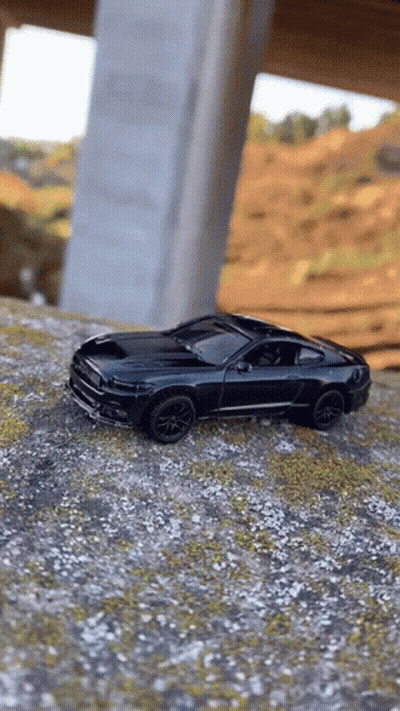 A Black Toy Car Is Sitting On Top Of A Dirt Hill Under A Bridge . GIF