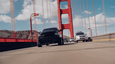 A Black Truck Is Driving Over A Bridge GIF