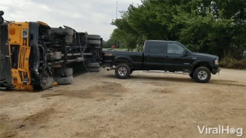 A Black Truck Is Towing A Yellow Truck On Its Side GIF