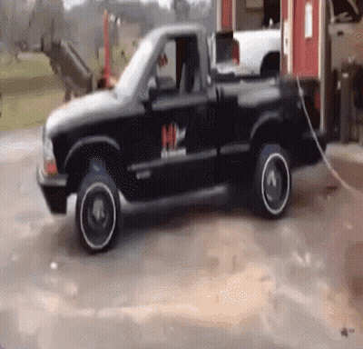 A Black Truck With A White Rim Is Parked In A Parking Lot GIF