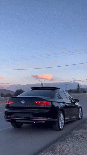 A Black Volkswagen Passat Is Parked On The Side Of A Road . GIF