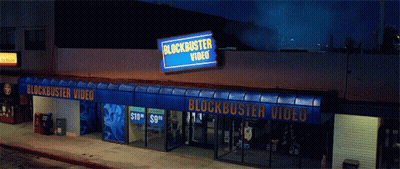 A Blockbuster Video Store At Night With A Blue Awning GIF