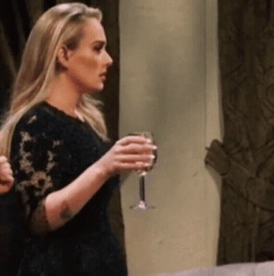 A Blonde Woman In A Black Dress Is Holding A Glass Of Wine . GIF