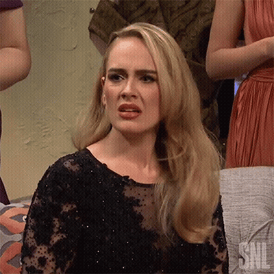 A Blonde Woman In A Black Dress Is Making A Funny Face While Sitting On A Couch . GIF