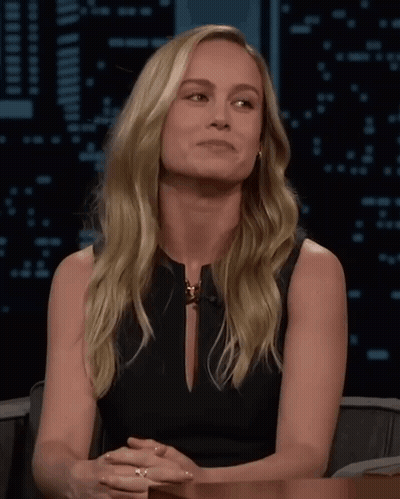 A Blonde Woman In A Black Dress Is Sitting At A Table GIF