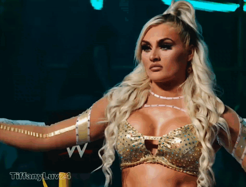 A Blonde Woman In A Gold Top With The Letters Vv On The Bottom GIF