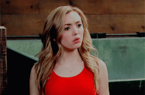 A Blonde Woman In A Red Tank Top Is Standing In Front Of A Wooden Fence GIF