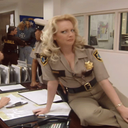 A Blonde Woman In A Sheriff 'S Uniform Sits At A Desk GIF