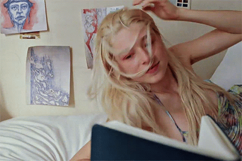 A Blonde Woman Is Laying On A Bed With A Book In Front Of Her GIF