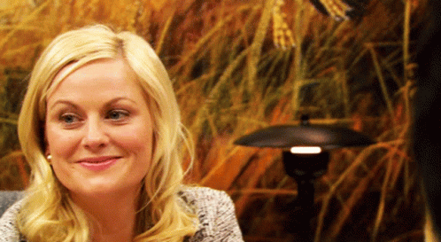 A Blonde Woman Is Smiling In Front Of A Painting GIF