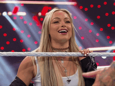 A Blonde Woman Is Standing In A Wrestling Ring Smiling . GIF