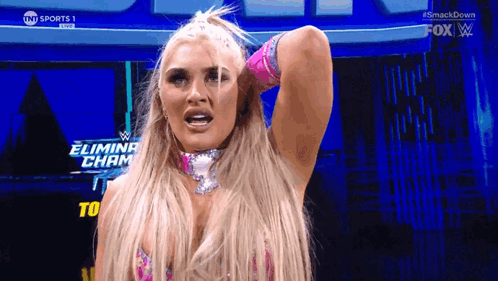 A Blonde Woman Is Standing In Front Of A Sign That Says Eliminate Champ GIF