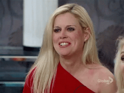 A Blonde Woman Is Wearing A Red One Shoulder Top And Smiling . GIF