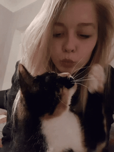 A Blonde Woman Kisses A Black And White Cat On The Nose GIF