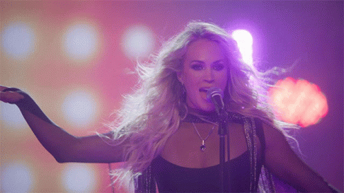 A Blonde Woman Singing Into A Microphone With Her Tongue Out GIF