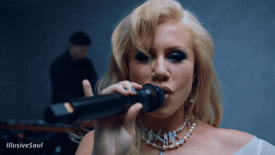 A Blonde Woman Singing Into A Microphone With The Words Illusive Soul Behind Her GIF