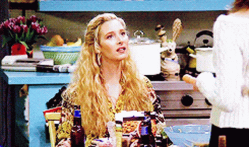 A Blonde Woman Sitting At A Table With Bottles Of Alcohol GIF