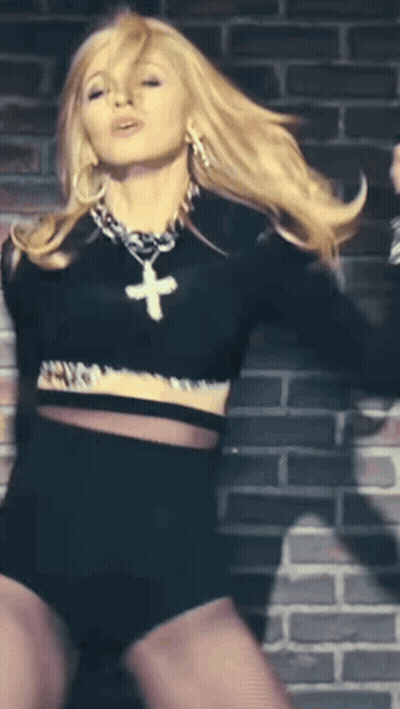 A Blonde Woman Wearing A Black Crop Top And Shorts With A Cross Necklace GIF