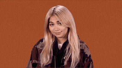 A Blonde Woman Wearing A Camouflage Jacket Looks At The Camera GIF