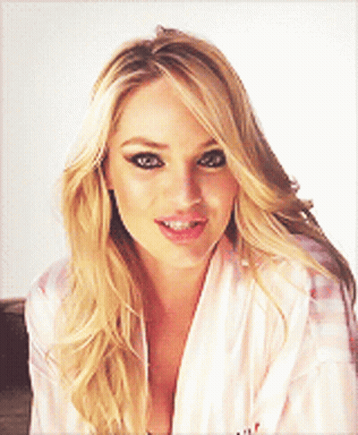 A Blonde Woman Wearing A Pink Robe Is Smiling And Looking At The Camera GIF