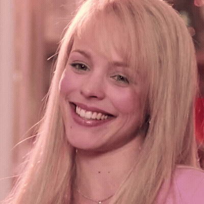 A Blonde Woman Wearing A Pink Shirt And A Necklace Is Smiling GIF