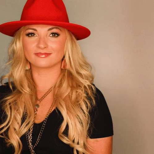 A Blonde Woman Wearing A Red Hat And Necklace GIF