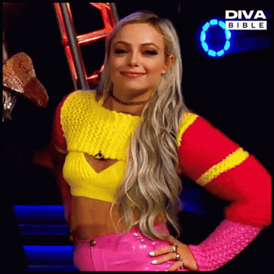 A Blonde Woman Wearing A Yellow And Pink Sweater And Pink Pants Is Standing In Front Of A Diva Bible Sign GIF