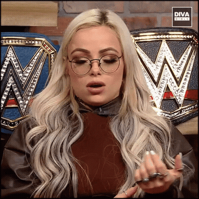 A Blonde Woman Wearing Glasses Is Standing In Front Of A Diva Branded Belt GIF