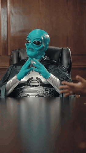 A Blue Alien Is Sitting At A Table With The Word But Visible GIF