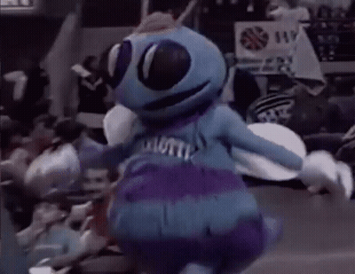 A Blue And Purple Mascot Is Dancing In Front Of A Crowd . GIF