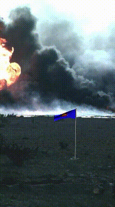 A Blue And Yellow Flag Is Flying In Front Of A Large Fire GIF