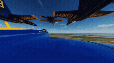 A Blue And Yellow U.s. Navy Jet Is Flying Over A Field GIF