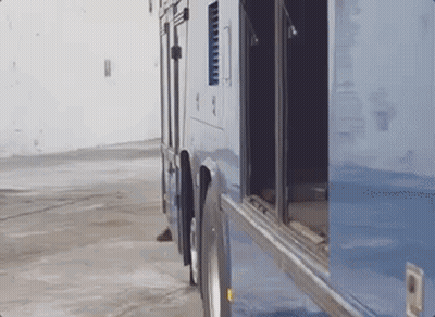 A Blue Bus With The Doors Open Is Parked In A Parking Lot . GIF