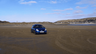 A Blue Car Driving On A Sandy Beach With A License Plate That Says Ykp Xkf GIF