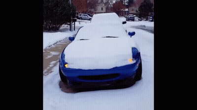 A Blue Car Is Covered In Snow On A Snowy Street GIF