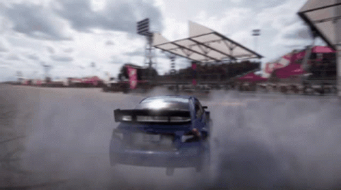 A Blue Car Is Drifting On A Track With Smoke Coming Out Of The Tires GIF