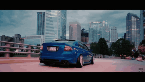 A Blue Car Is Parked On A Bridge In Front Of A Skyline GIF
