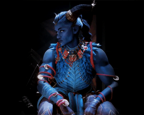 A Blue Demon With Horns And A Necklace Is Sitting In The Dark GIF