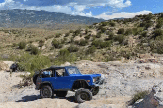 A Blue Jeep Is Parked On A Rocky Hillside With Mountains In The Background GIF