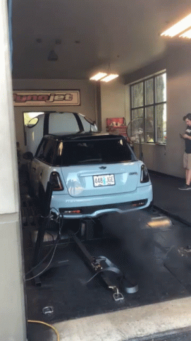 A Blue Mini Cooper Is Being Tested In A Garage With A Sign That Says Tunejet GIF