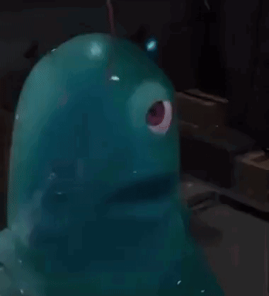 A Blue Monster With A Red Eye Is Sitting On A Table In A Dark Room . GIF