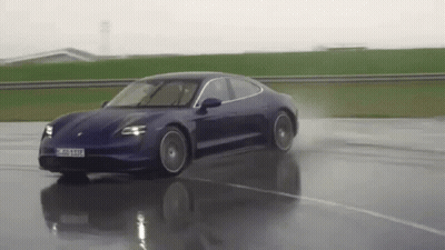 A Blue Porsche Taycan Is Driving Down A Wet Road . GIF