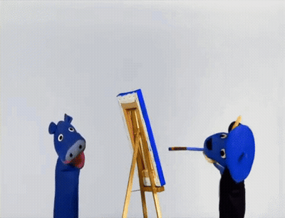 A Blue Puppet Is Painting A Picture On An Easel GIF