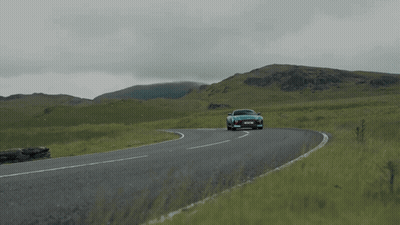 A Blue Sports Car Is Driving Down A Road With Mountains In The Background And A License Plate That Says Ycs Jml GIF